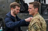 Journalist helps airman put on a microphone for an interview