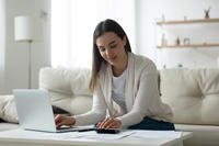 Woman Reviews Finances Using Paper Documents, a Calculator and a Laptop