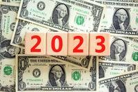 wooden blocks spelling out 2023 sitting atop pile of one dollar bills