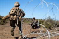 A Marine walks through an opening in a concertina wire obstacle during training.