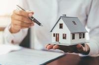 A stock image cropped tightly hands holding the model of a house and a pen.