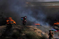 Palestinian demonstrators wave their national flags while others burn tires.