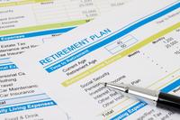 Printouts listing aspects of retirement planning arrayed on with a silver-colored pen weighing them down.