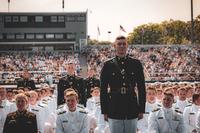 Amid white-jacketed military academy graduates, dark-jacketed graduates stand in recognition.