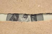 The eyes of a president on paper money peek through the rip in a piece of brown paper.