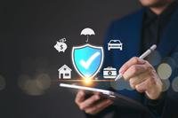 A hand holding a pen appears to be checking items on a list amid graphic icons representing forms of insurance.