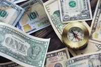 A mix of different U.S. bills are jumbled around a desktop with a brass-colored compass.