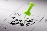 Zoomed in to the 20th on a generic calendar page, the words &quot;pay off debt&quot; appear handwritten in black marker near a thumbtack.