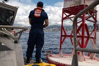 A Coast Guardsman stands on the forward deck of a 45-foot response boat-medium and prepares to handle line on a channel marker buoy outside of the Honolulu harbor entrance.