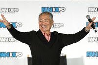 George Takei smiles with his arms outstretched while speaking onstage at Fan Expo Vancouver 2019