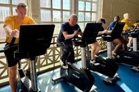 Navy members in PT uniforms ride stationary bikes.