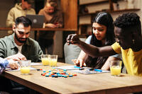 A group of friends playing a board game together at a table with drinks.