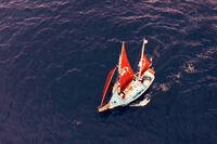 Aerial view of the Golden Rule sailing across open water with red sails in a scene from the documentary.