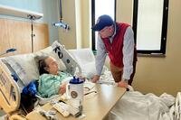 The VA secretary leans over the bed of a hospital patient as the two regard each other eye to eye.