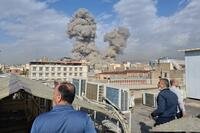 People watch as smoke rises on the skyline after an explosion in Tehran, Iran.