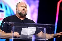 Alex Jones stands behind a clear podium and speaks at a public event. Photo Credit: Source: Wikimedia Commons/Public domain