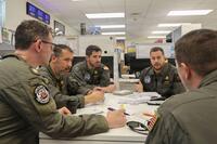 Men in flight suits around a table.