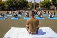 A soldier leads a field of soldiers on yoga mats in a seated yoga pose.
