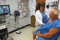 Army Veteran Herbert Lang (seated, right) is examined by his Lovell FHCC cardiologist Dr. Eric Yeung (on screen) during a follow-up appointment at the McHenry Community Based Outpatient Clinic. (DoD photo)