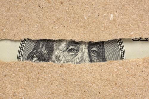 The eyes of a president on paper money peek through the rip in a piece of brown paper.