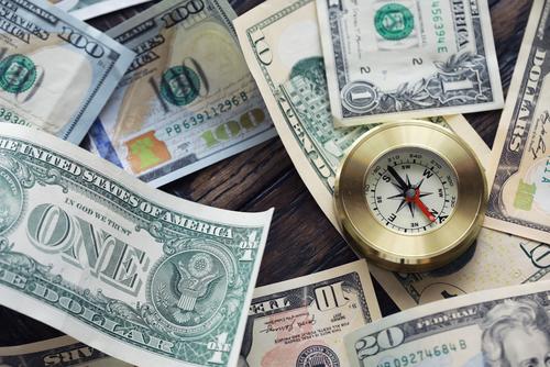 A mix of different U.S. bills are jumbled around a desktop with a brass-colored compass.
