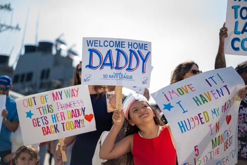Navy kids wave welcome home signs.